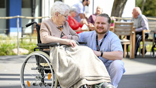Ehrenamtler aus der Altenpflege kümmert sich um eine Seniorin im Rollstuhl.